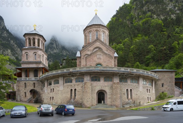Historic monastery building surrounded by mountains and clouds in a peaceful atmosphere, Dariali