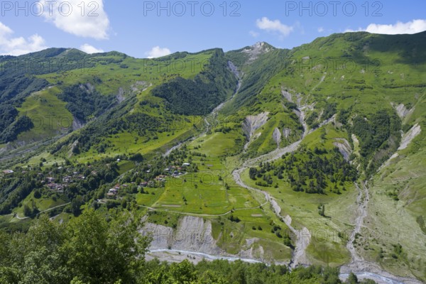 Green valley with mountains and river under blue sky and few clouds, viewpoint near Gudauri, view