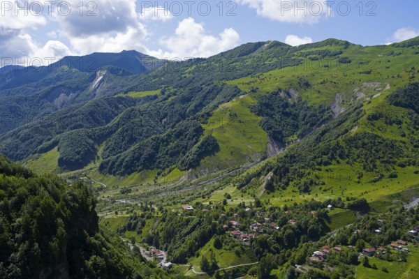 Lush green mountains with scattered village under blue sky and clouds, viewpoint near Gudauri, view