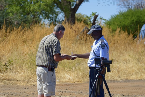 A police officer talks to a man on the side of the road in a rural setting, man must pay fine for