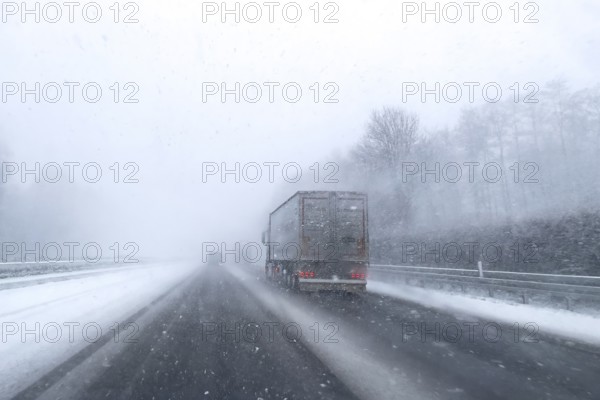 View through the windshield of a passenger car driving through light snowblowing on partly
