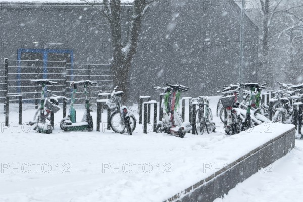 Tailored parked e-scooters and bicycles in winter during snowfall with snowflakes in the picture,
