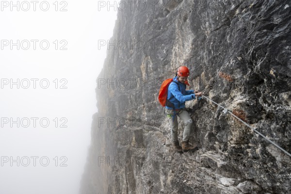 Mountaineers on a steep rock face on the Via Ferrata Oliva Detassis via ferrata in fog, steep