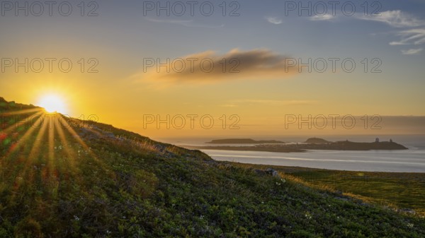 Midnight sun on Mount Domen in the background the city of Vardø, sea at sunset with golden sky and