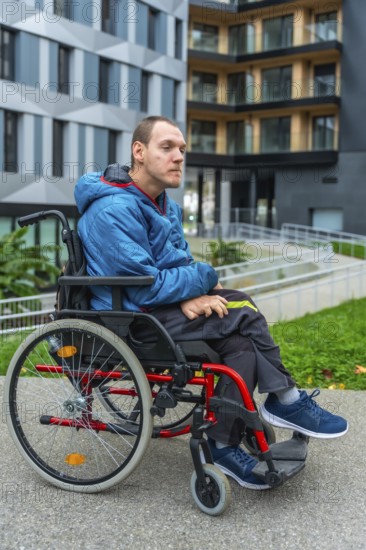 Young man living with a disability sitting in a manual wheelchair on a paved path outside modern