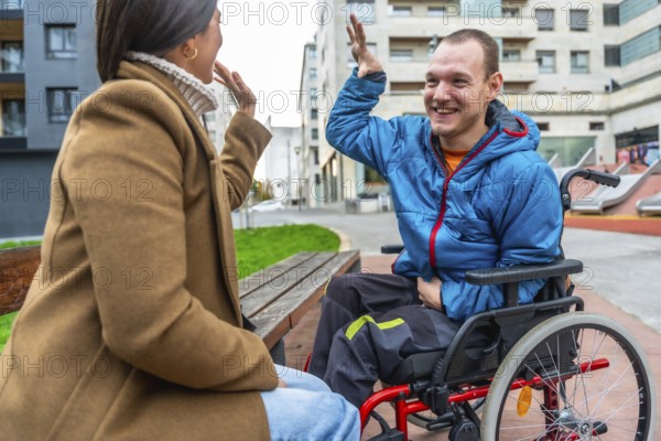 Joyful disabled man in a red wheelchair sharing a high five with a woman on a bench, symbolizing