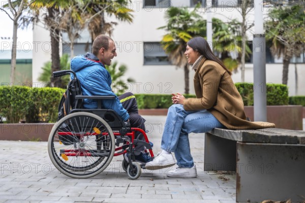 Man with a disability in a wheelchair having a cheerful conversation with a woman sitting on a park