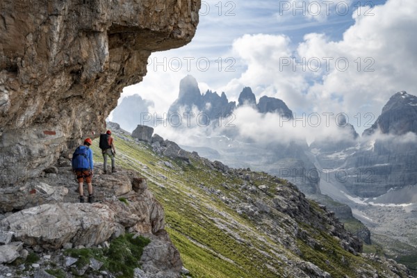 Two mountaineers on a path in front of a picturesque mountain landscape with rocky peaks, Via