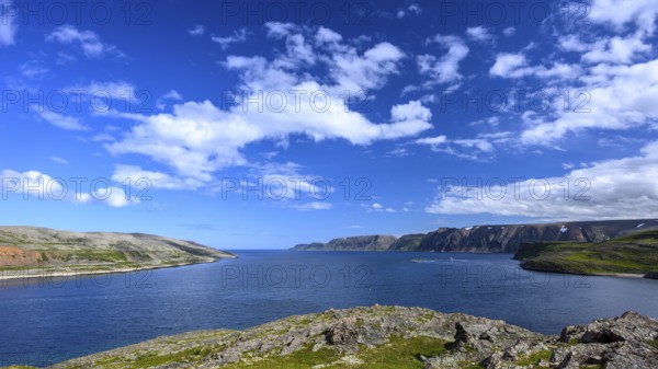 Green meadows on the banks of Syltefjord with clouds in the blue sky, landscape with a lake and