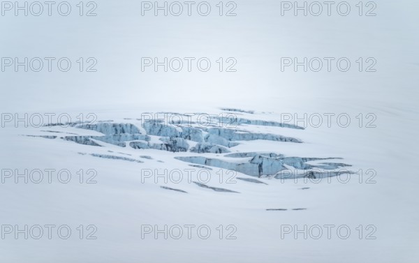 Smooth white snowy area on the glacier broken by crevasses with blue rugged glacial ice, detail,