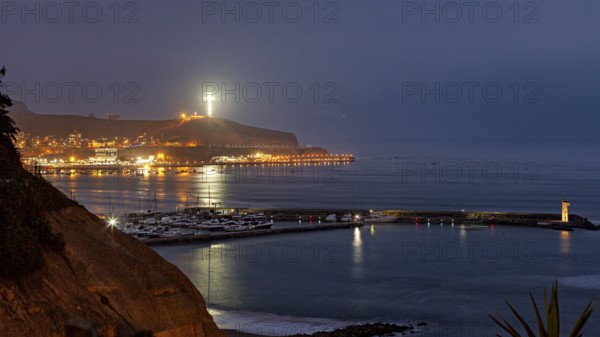 Coastal landscape at night with illuminated cross on a hill and harbor lights, calm sea atmosphere,