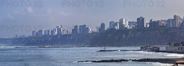 View of a coastal town with skyscrapers on cliffs and waves under a blue sky, The coast with the