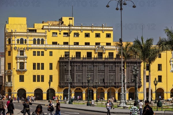 Yellow colonial building with wooden balcony on a busy street with strolling people, the historic