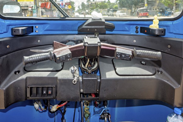 The picture shows the cockpit of a blue car rickshaw in an urban environment, the cockpit of a tuk