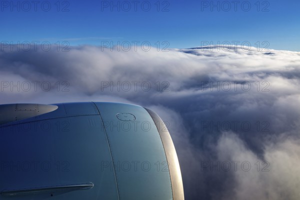 View from an airplane window of an engine and underlying clouds in the blue sky, on the plane above