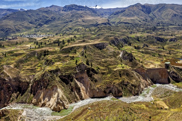 Mountain landscape with terraced fields and a river surrounded by green nature under blue skies,