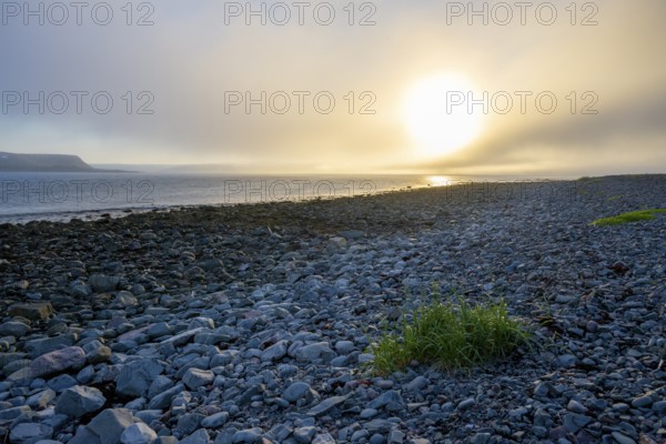 A peaceful beach at sunset with rocks and calm sea under a slightly cloudy sky, Båtsfjord,