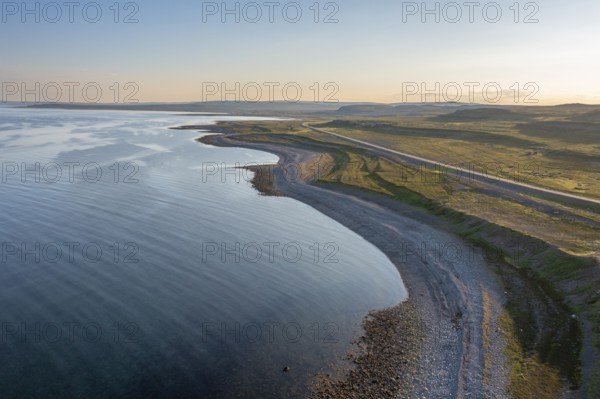 Coastal landscape on Varangerfjord with blue sky, still sea, moors and pebble beach aerial view,