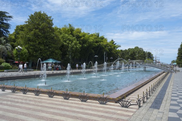 Fountain with walkway and trees in urban landscape under blue sky, Batumi Boulevard, Batumi, Black