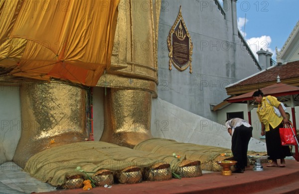 Women place flowers on standing Buddha's toes at Wat Indrawihan, Bangkok, Thailand, December 2002,
