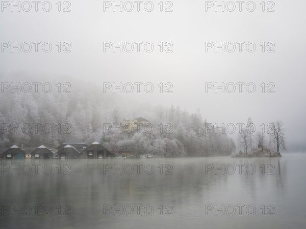 View across Königssee to boathouses, Christlieger island and frozen trees in fog, Schönau am