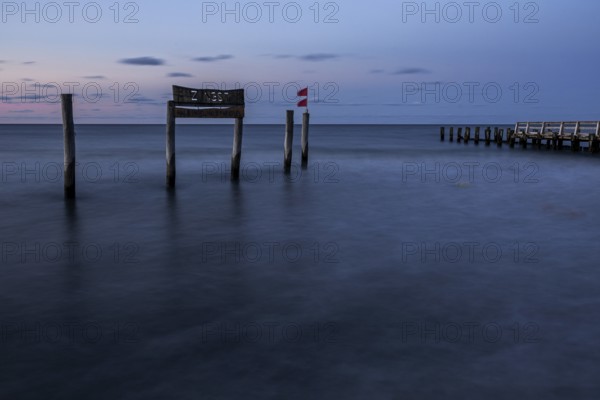 Wooden sign in the sea with inscription Zingst and wooden walkway, long exposure, evening light,
