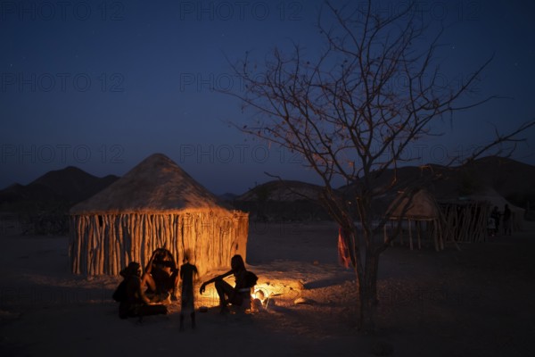 Himba at the campfire in the evening, night view, Himba huts, traditional Himba village in the