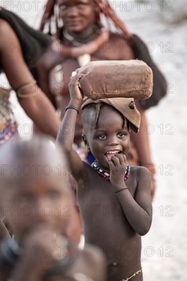 Himba woman and children run to fetch water with canisters through dry countryside, traditional