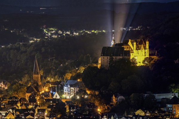 Castle and church shine in night lighting on a wooded hill. The Landgrave's Castle of Marburg in