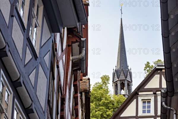 View of a narrow street with half-timbered houses and a church tower in the background, The