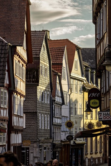 Narrowly built street with historic half-timbered houses and people passing by in the evening
