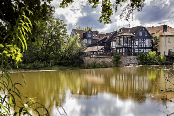 Half-timbered houses are reflected in the water in partly cloudy skies. The historic houses of