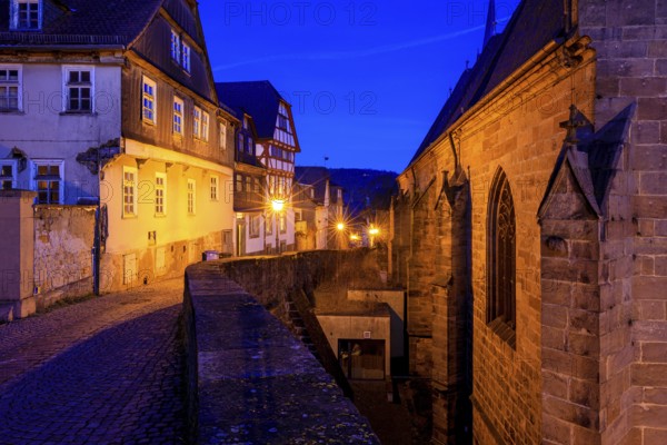 Historic street view at dusk with illuminated half-timbered houses and a church building, At the