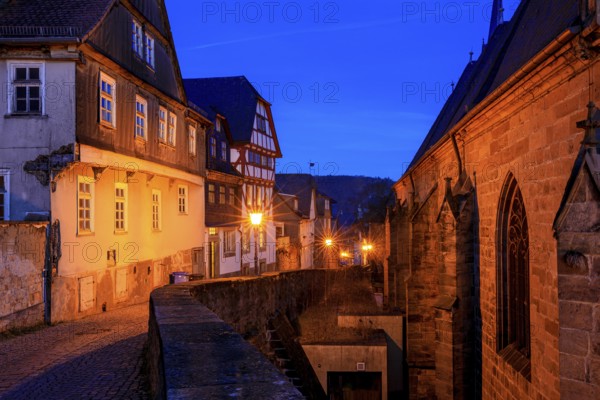 A nocturnal old town with half-timbered houses and cobblestones, warm lantern light creates a