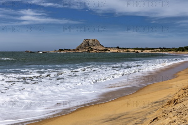 A peaceful coastal scene with sandy beach, turquoise ocean and distant rocks under blue skies, the
