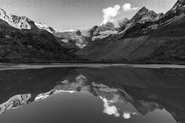 The Moiry glacier and mountain peaks are reflected in Lac de Chateaupre, black and white photo, Val