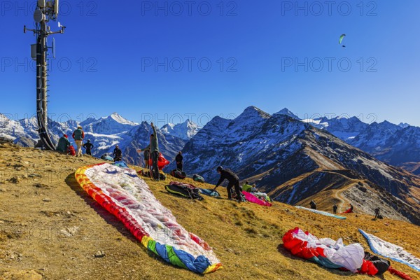 Paragliders are preparing for their start, with the snow-capped peaks of the Valais Alps, Val