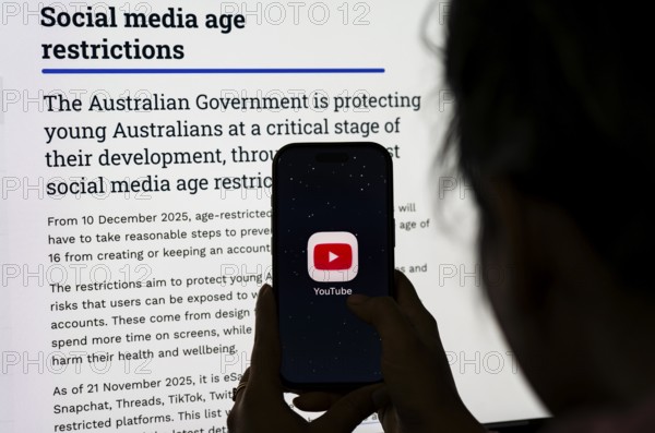 In this photo illustration, a person holds a phone displaying the YouTube app in front of a screen