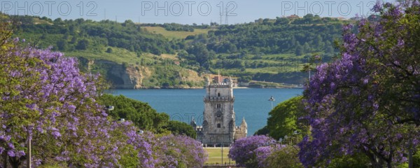 Scenic view of Belem Tower in Lisbon, Portugal, seen over a street with blooming purple jacaranda