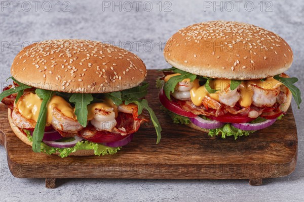 Two shrimp burgers and buns with sesame seeds, bacon, lettuce, tomatoes and onions, On a wooden