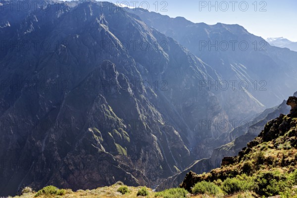 Deep canyon surrounded by high mountains in sunlight with shady areas, the mountains and valleys of