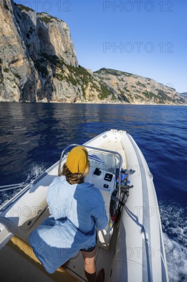 Young woman riding a motorboat along the picturesque rocky coast, cliffs and blue sea, Golfo di
