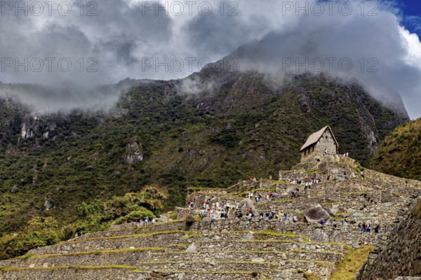 Stone structures on steep terraces in front of a cloudy mountain, The ruins of the Inca city of