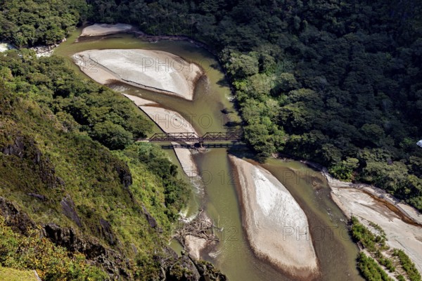 Aerial view of a river with sandbanks and a bridge surrounded by thick forest, view of the Urubamba