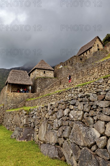 Stone walls and traditional houses against a dramatic, cloudy sky, the ruins of the Inca city of