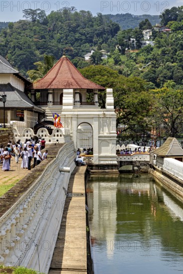 A temple with a pavilion near a river, with people and green surroundings, The Temple of the Tooth