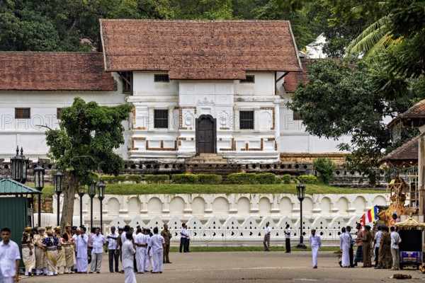A temple with red roof and white walls surrounded by people and trees, The Temple of the Tooth in