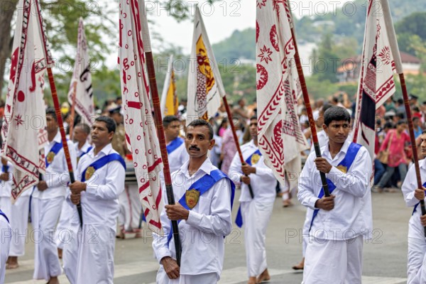 Participants wearing festive white uniforms carry red and white flags in a celebratory parade, The