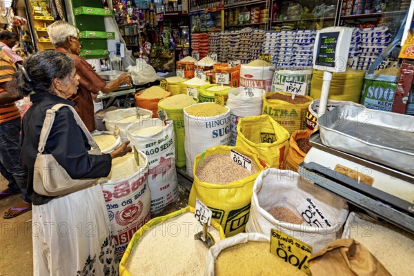 Market customers buy rice from large bags at a well-stocked stand, dealers in the market halls of