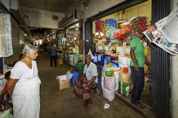 Elderly woman and salesman in a market aisle with colorful goods and packaging, dealer in the